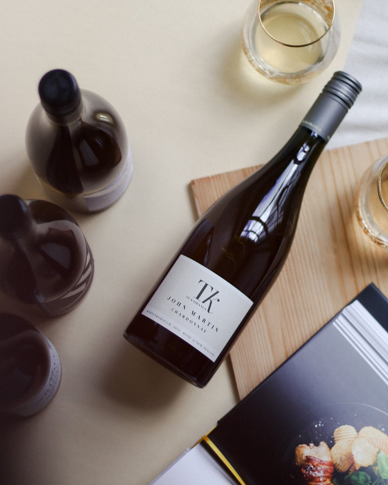 Wine bottle with a glass of white wine on a table with a menu and other items.